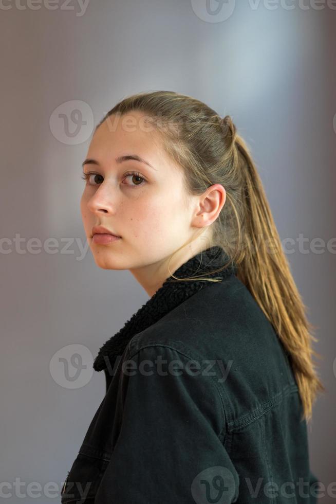 Trois quarts tourné ou portrait de profil semi d'une jolie adolescente avec des cheveux de queue de cheval posant en regardant la caméra sur un fond gris photo