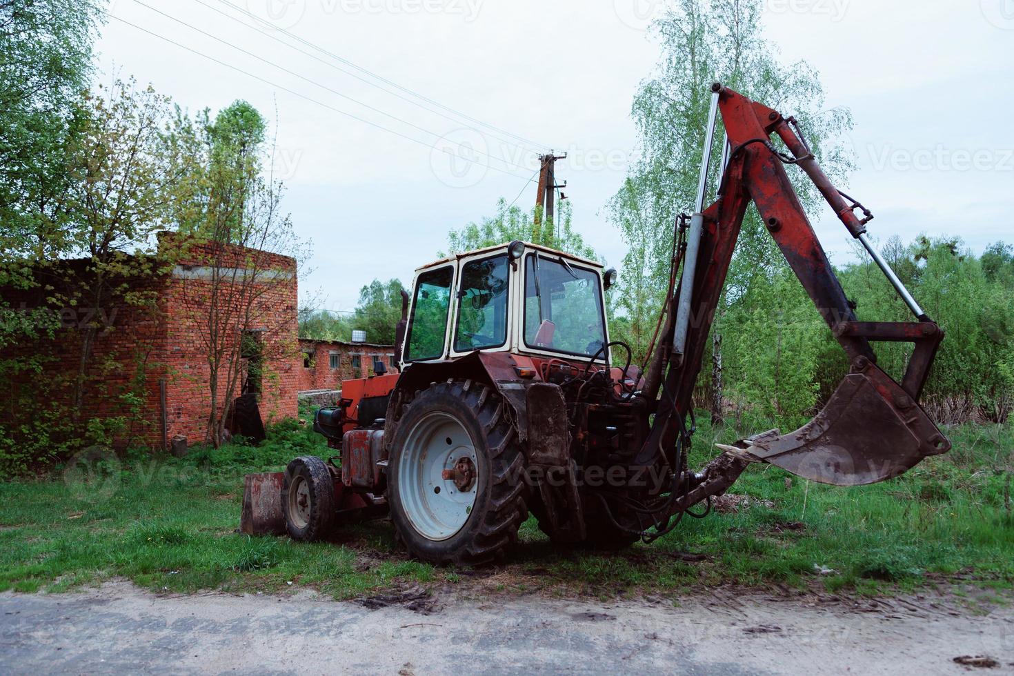 Vieux tracteur rouillé rouge dans un champ près de la route photo