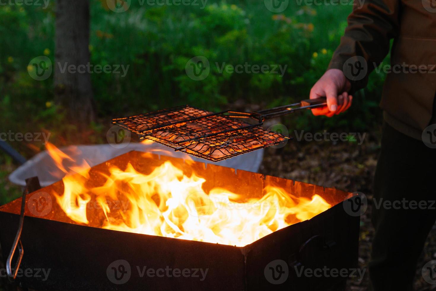 Une main d'homme tient un gril en fer avec une brochette de saucisse sur le feu photo