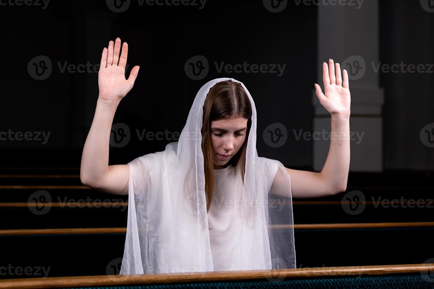 une jeune fille modeste avec un mouchoir sur la tête est assise à l'église et prie photo