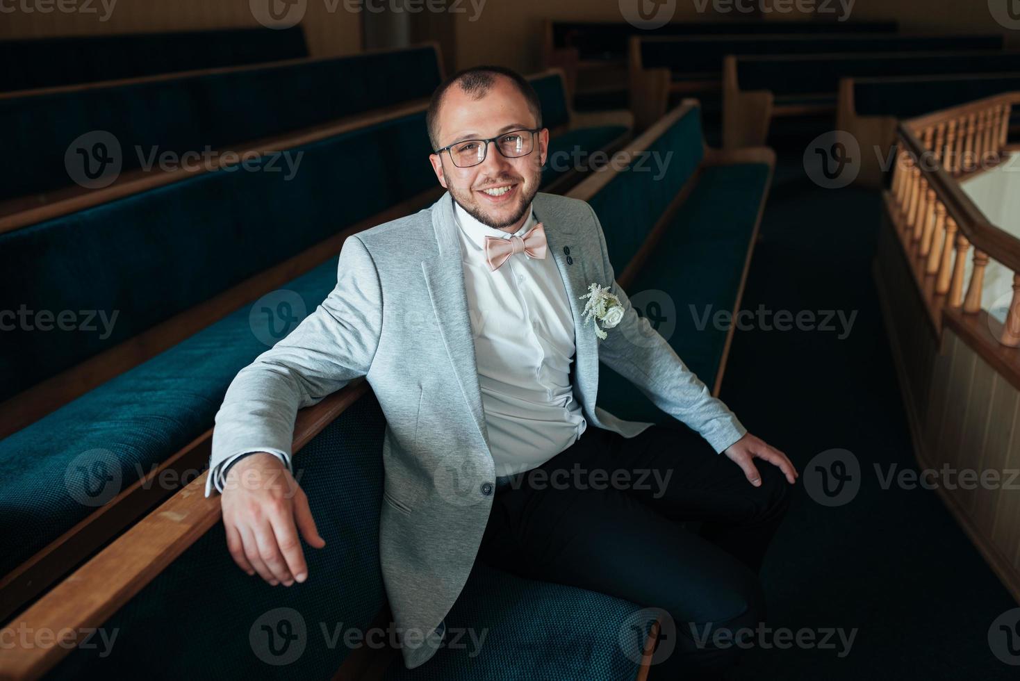 Photo de mariage des émotions d'un marié barbu avec des lunettes dans une veste grise dans le bâtiment de l'église