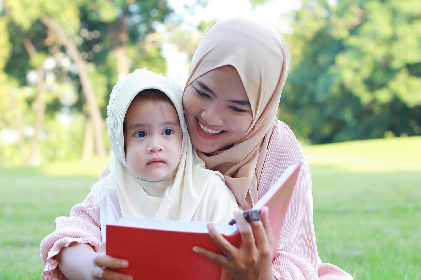 mère musulmane apprend à sa fille à lire joyeusement le coran dans le parc en été photo