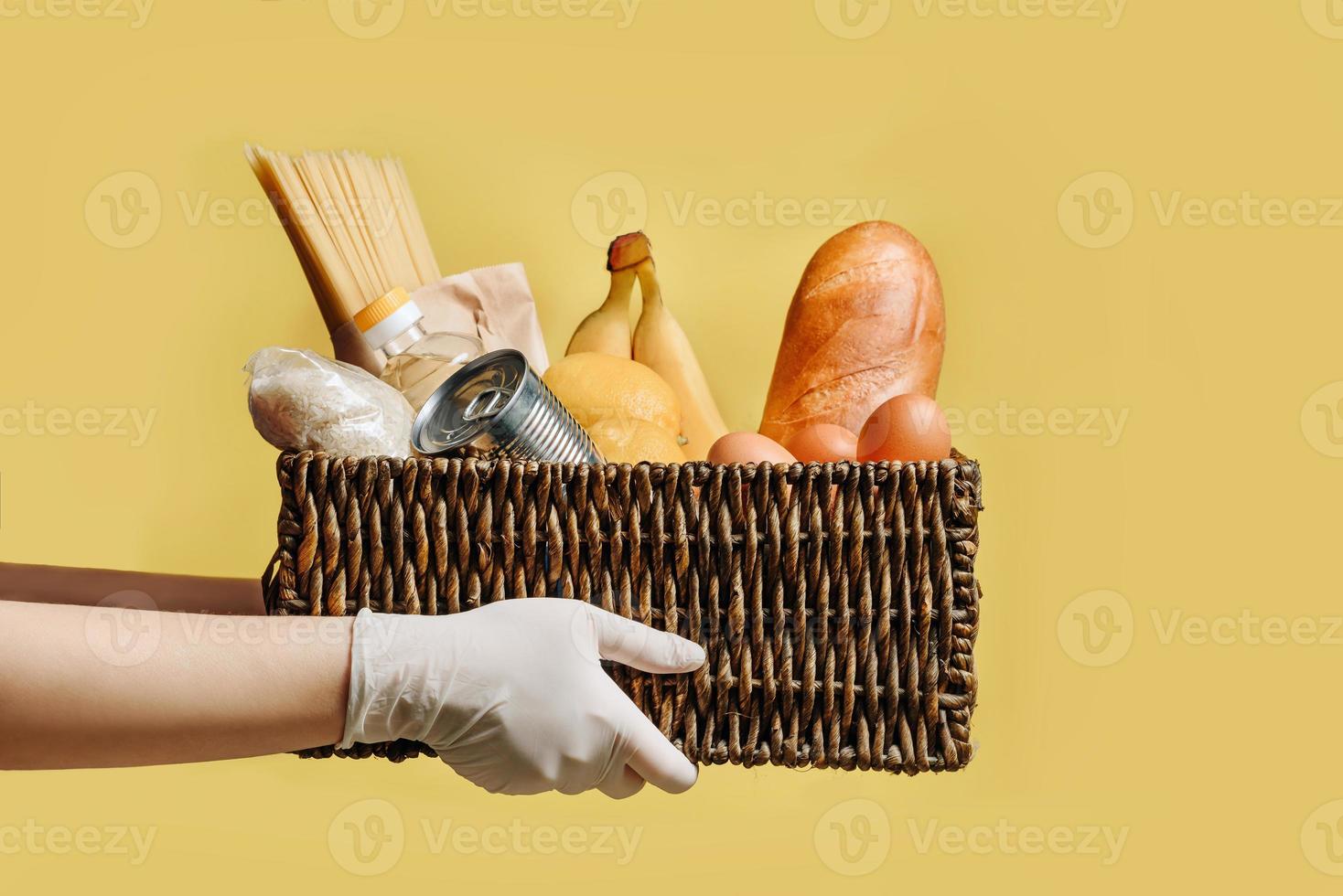 Panier en osier avec un ensemble de produits dans les mains dans des gants de protection isolés sur fond jaune photo