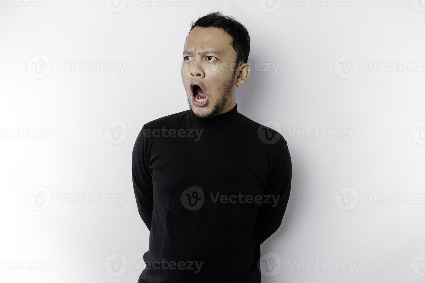 sous le choc asiatique homme avec le sien bouche large ouvert portant noir chemise, isolé par une blanc Contexte photo