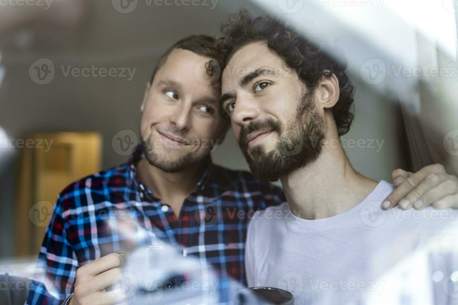 Jeune gay couple dans l'amour à la recherche en dehors le la fenêtre. deux Jeune androgyne Hommes souriant ensemble et ayant café. photo