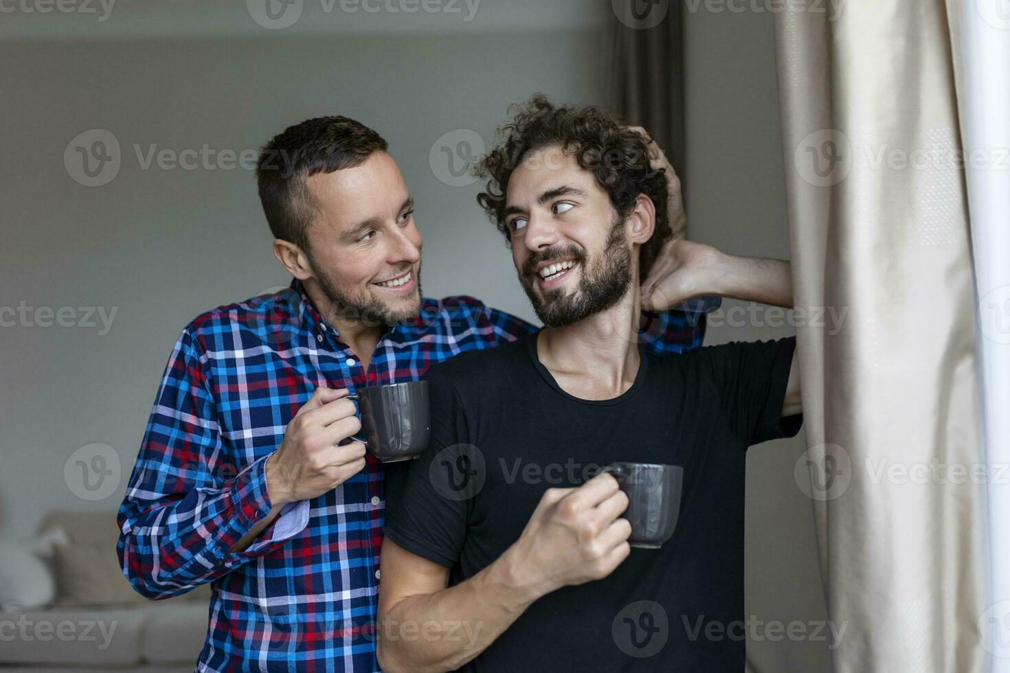 Jeune gay couple dans l'amour à la recherche en dehors le la fenêtre. deux Jeune androgyne Hommes souriant ensemble et ayant café. photo