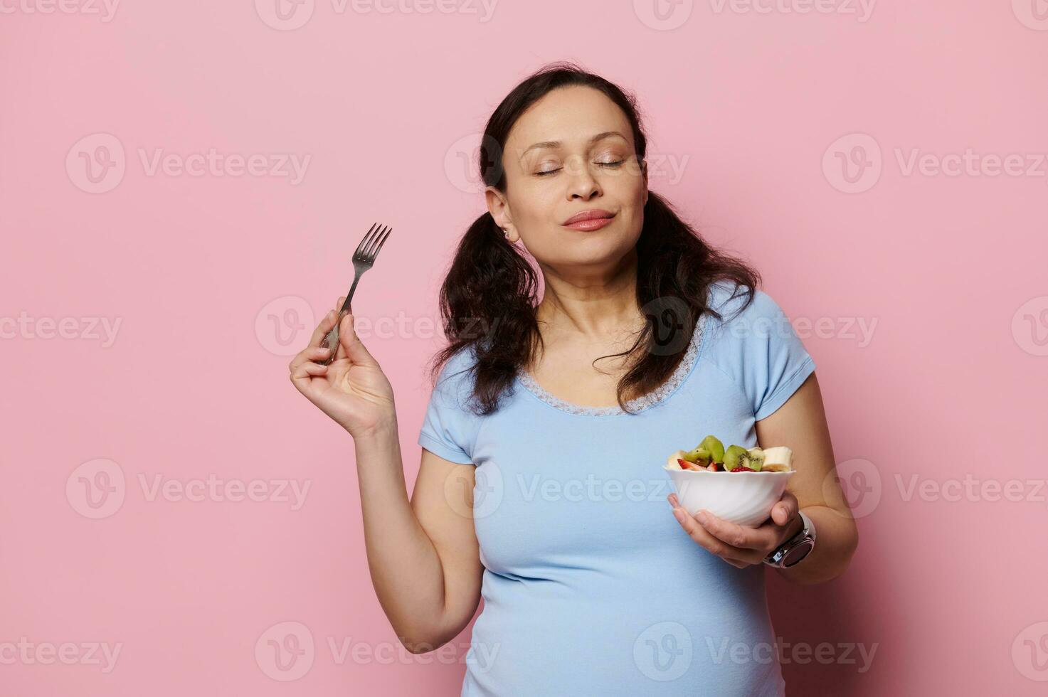 délicieux femme enceinte Enceinte femme en mangeant des fruits salade, isolé rose Contexte. en bonne santé nutrition dans grossesse temps photo