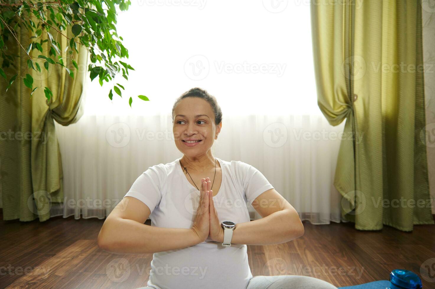 multi ethnique Enceinte femme étreinte mains, souriant à la recherche de côté blanc pratiquant grossesse souffle des exercices à l'intérieur photo