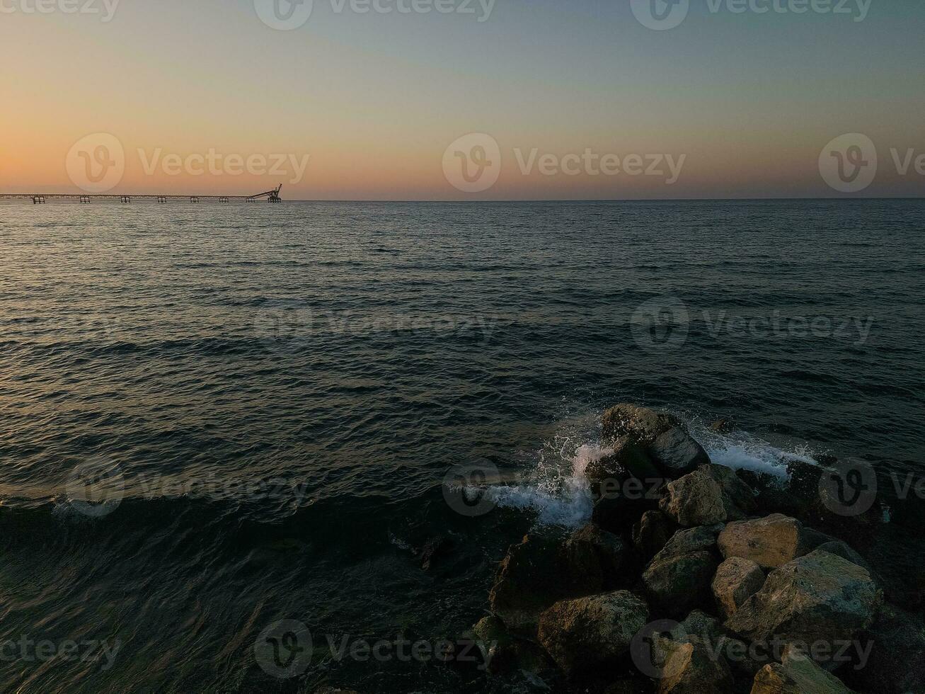 paysage marin avec écrasement vagues et vieux déserté industriel jetée dans le distance à le coucher du soleil à karavostasi zone près lefka, Chypre. photo