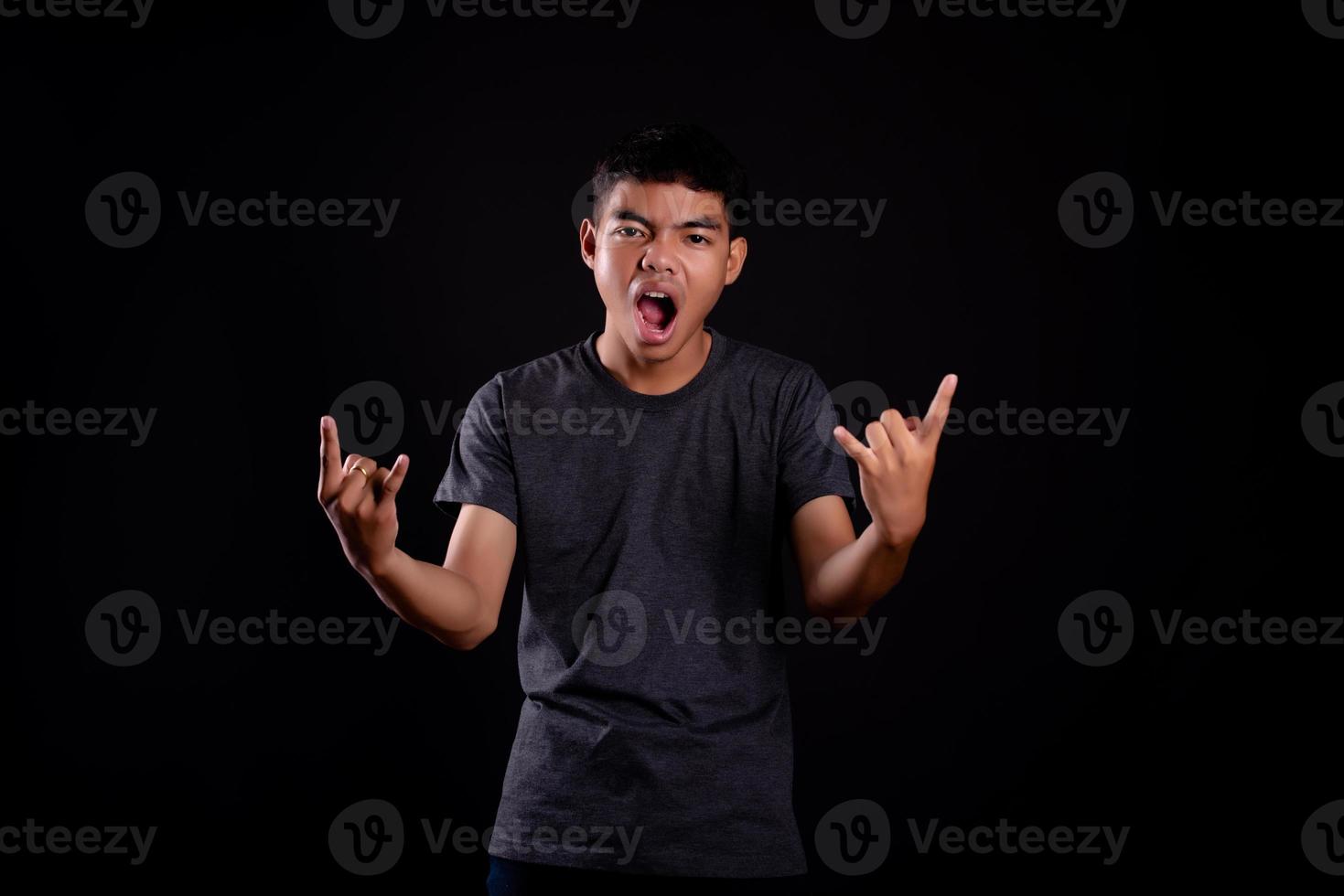 Jeune homme en veste de cuir noir avec guitare électrique sur fond noir en studio photo