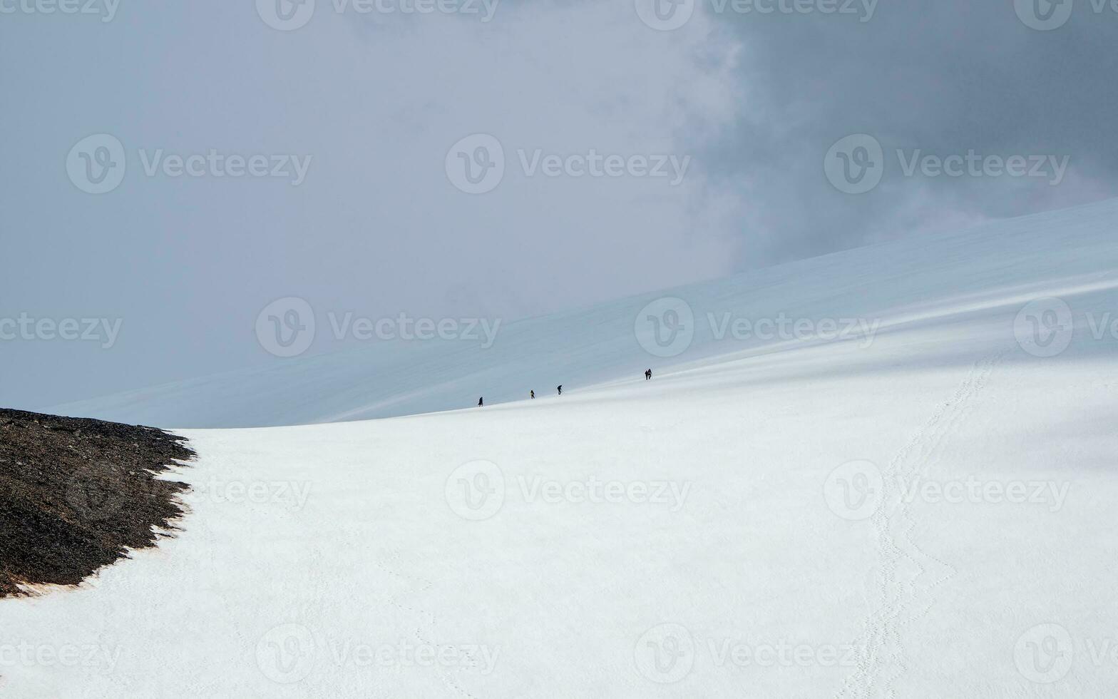 minimaliste panoramique paysage avec groupe escalade sur grand neigeux Montagne dans lumière du soleil en dessous de nuageux ciel. atmosphérique paysage avec ensoleillement sur haute neige Montagne à changeable temps. photo