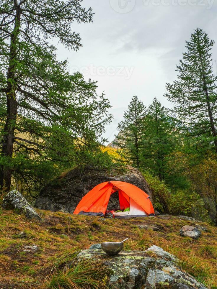 vide touristique bol avec une cuillère est posé en dehors sur une pierre contre le Contexte de une Orange tente et forêt avec haute montagnes. le déjeuner temps, haute altitude randonnée. photo