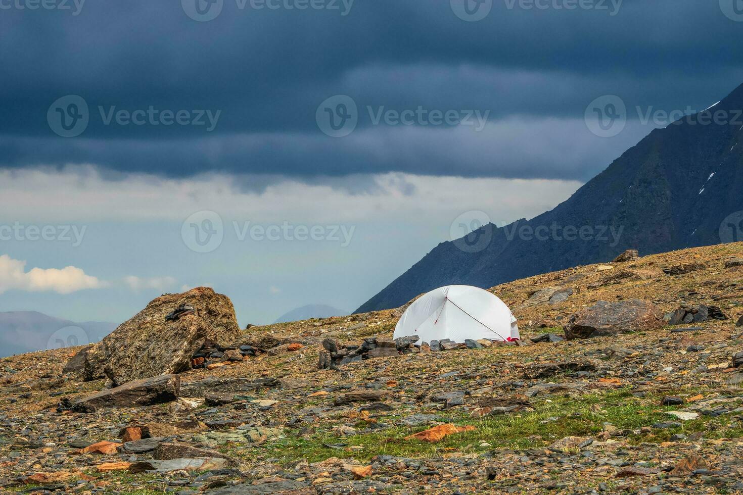 camping sur une rocheux haute altitude plateau. blanc tente sur le Contexte de glacier et haute enneigé montagnes. solo randonnée concept. solitude dans la nature. photo
