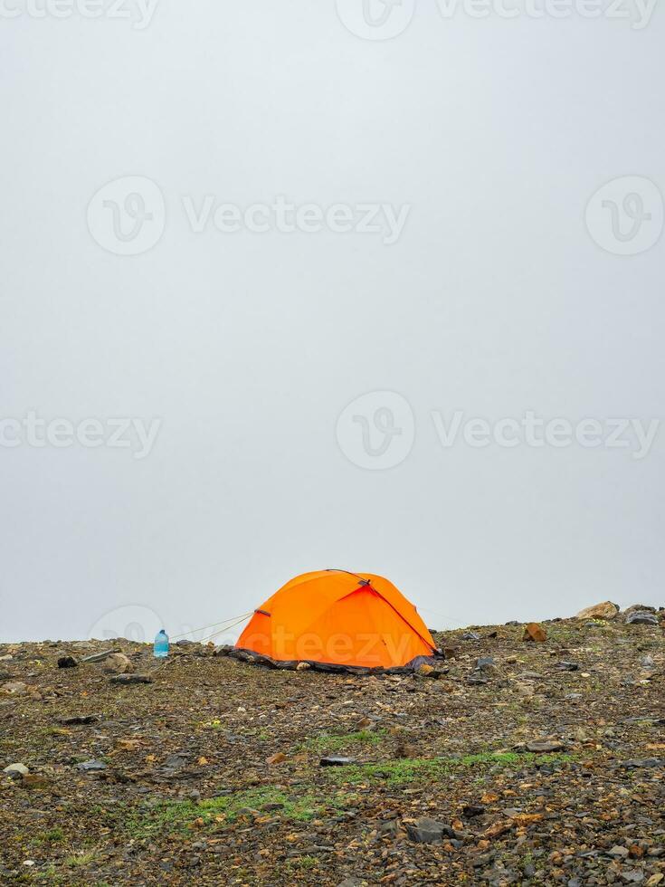 scénique alpin paysage avec Orange renforcé tente contre le Contexte de une glacier sur une haute altitude plateau. Voyage concept. verticale voir. photo