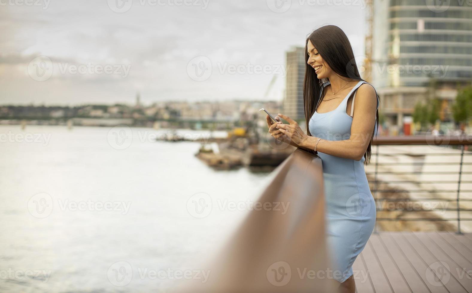 jeune femme à l'aide d'un téléphone mobile en se tenant debout sur la promenade du fleuve photo