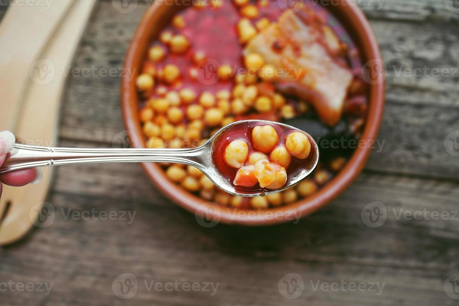 Plat de saucisse de pois chiches et bacon dans une mijoteuse par cuillère et fourchette en bois photo