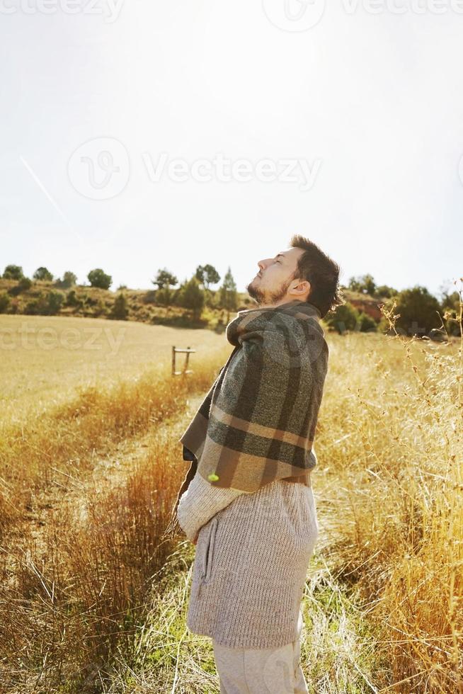 Côté d'un stand jeune homme profitant dans le calme du soleil d'automne du matin dans un chemin d'un champ jaune avec le contre-jour du ciel bleu photo