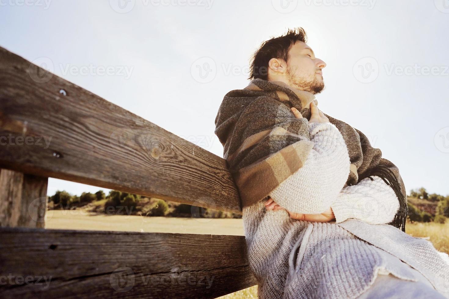 Face latérale d'un jeune homme aux yeux fermés appréciant dans le calme le soleil d'automne du matin dans un champ jaune avec le contre-jour du ciel bleu photo