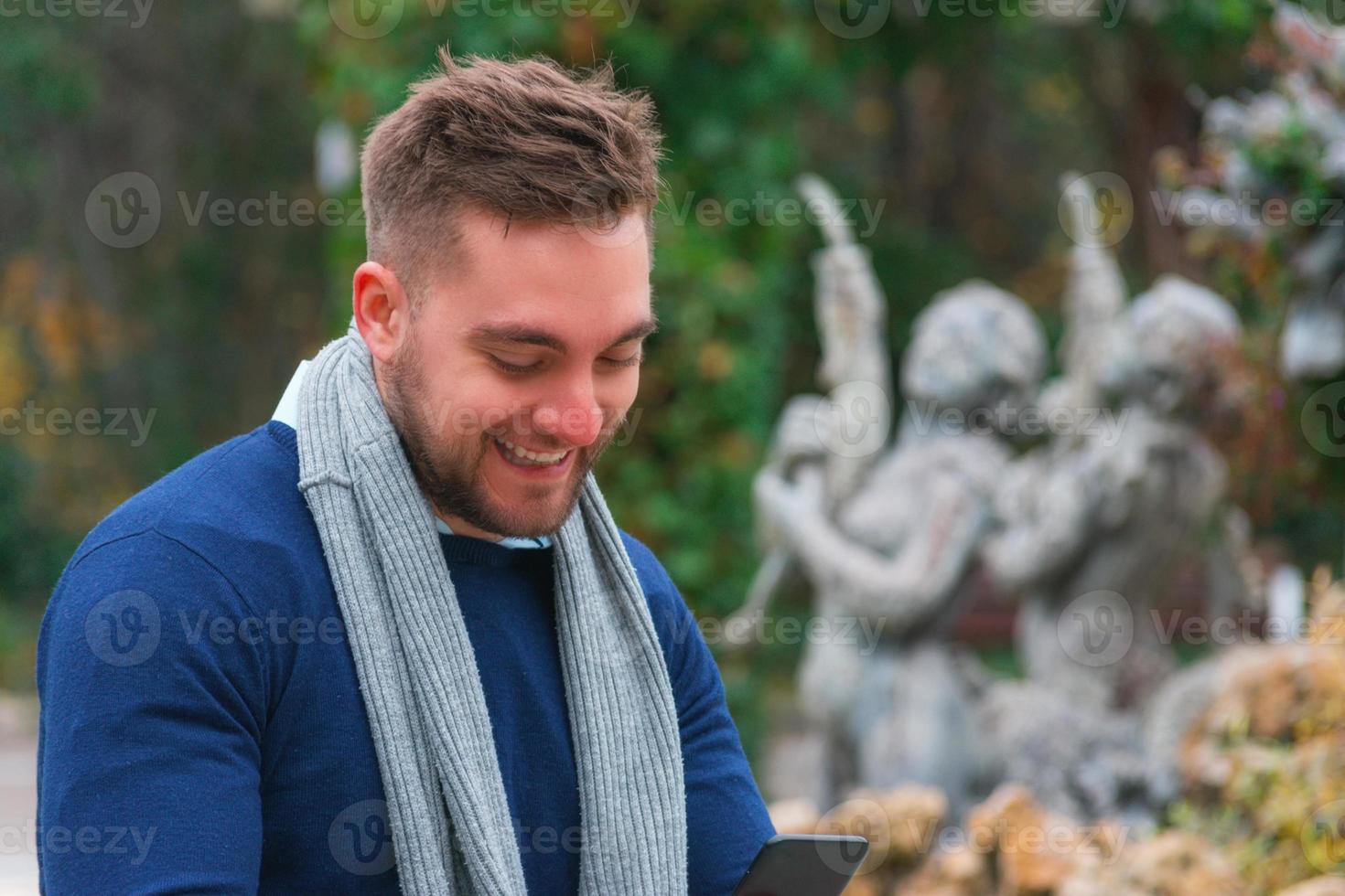 jeune homme souriant dans un parc vérifiant son téléphone portable photo