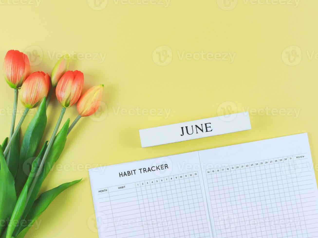 plat allonger de habitude traqueur livre avec en bois calendrier juin, et tulipes sur Jaune Contexte. photo