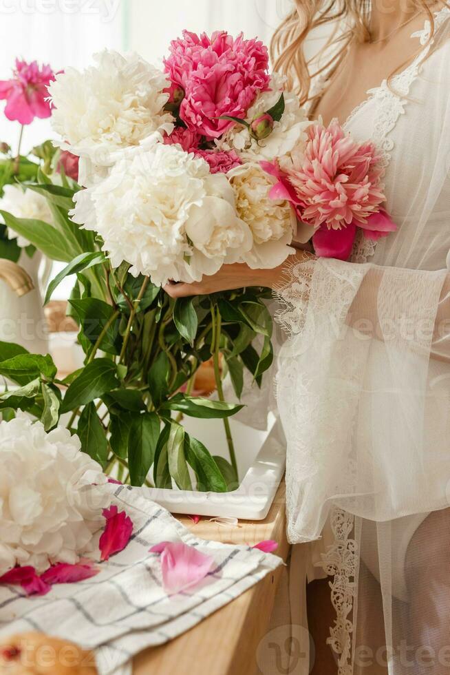 le cuisine plan de travail est décoré avec pivoines. le intérieur est décoré avec printemps fleurs. rose pivoines et sucré petits gâteaux sur une en bois comptoir. intérieur détails. photo