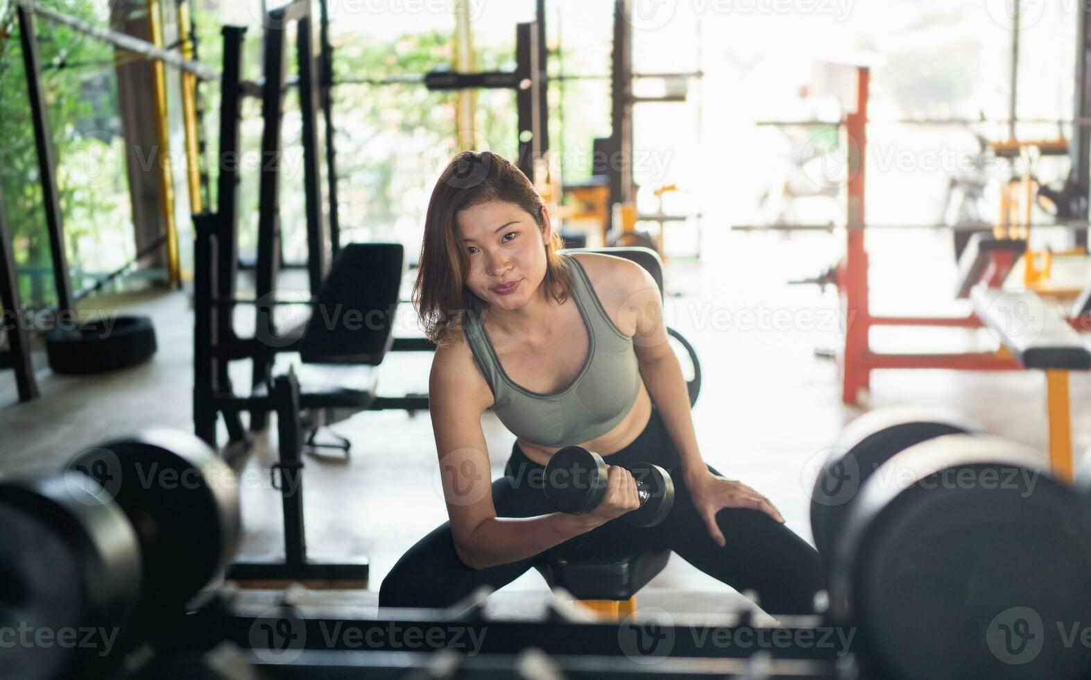 sportive asiatique en forme souriante et travaillant sur des poids d'exercice avec des haltères à la salle de fitness. femme asiatique portant des vêtements de sport faisant de l'exercice pour brûler les graisses au gymnase. concept de fitness femme sport. photo