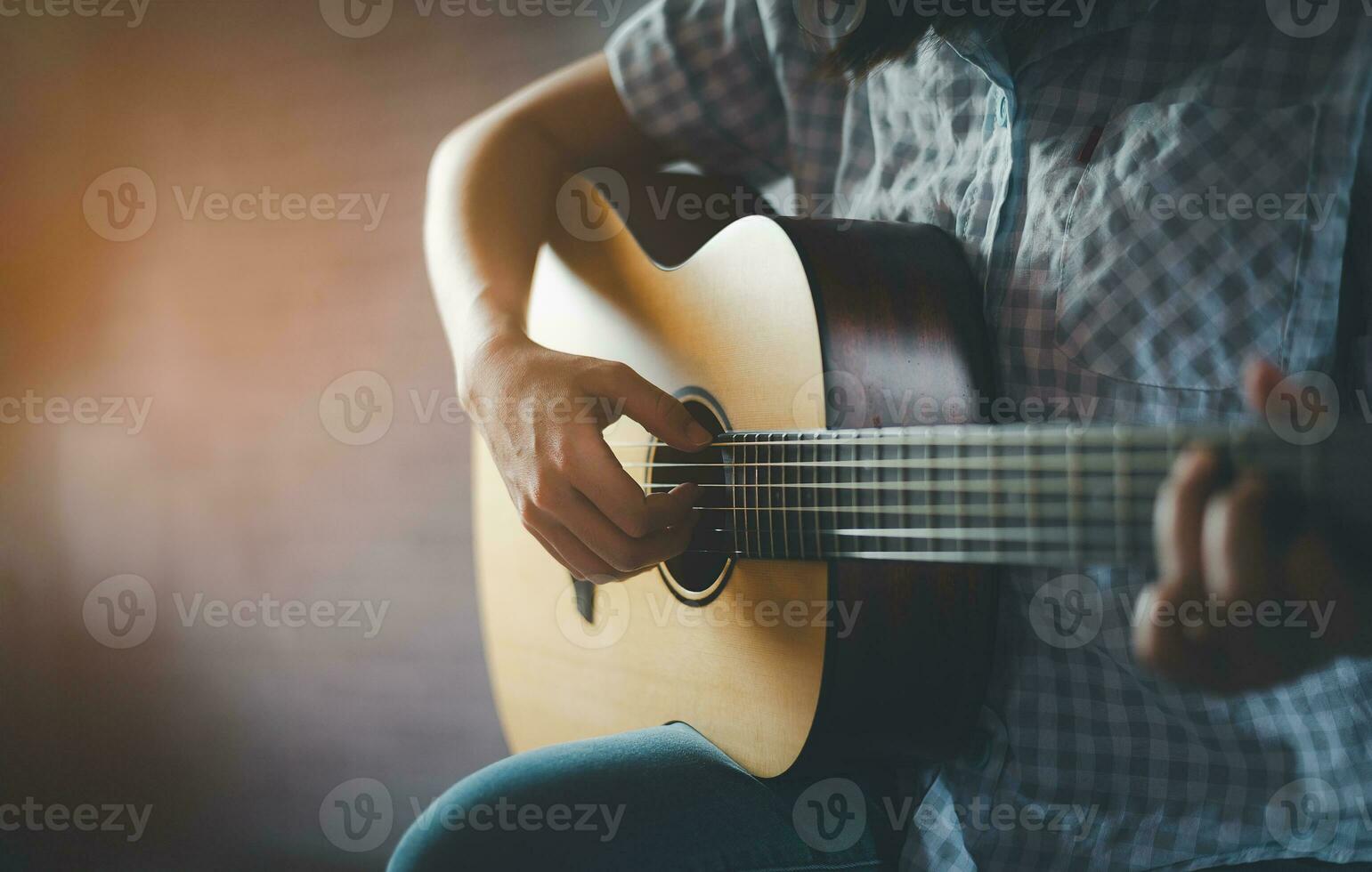 femme en jouant acoustique guitare séance dans Publique parc dans une détendu. femme pratiquant en jouant guitare en dessous de une arbre Heureusement. photo