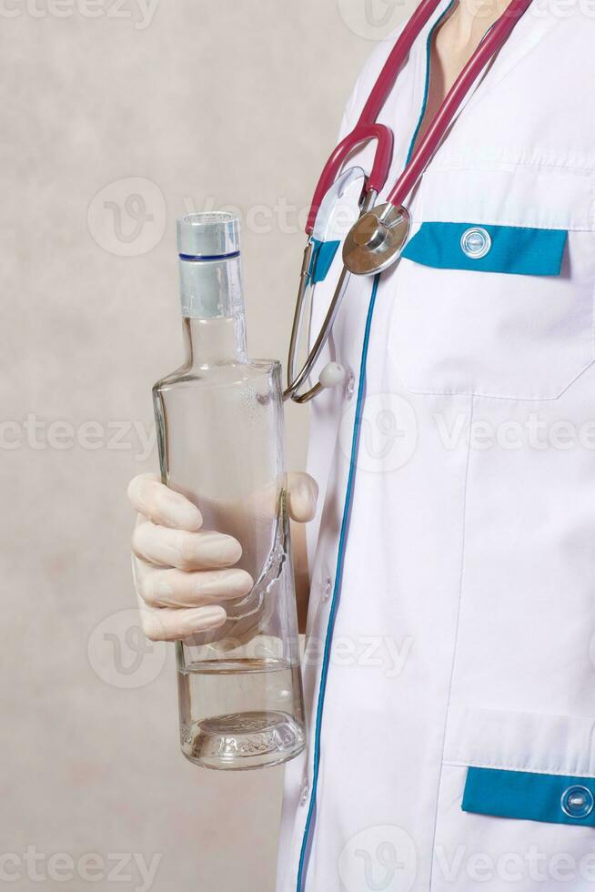 une Jeune femme habillé dans une médical uniforme garde une bouteille de alcool. fermer photo