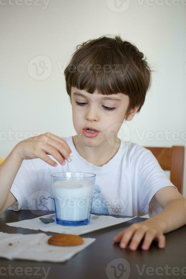 garçon de six ans est prise une verre de chaud Lait avec avoine des biscuits. photo