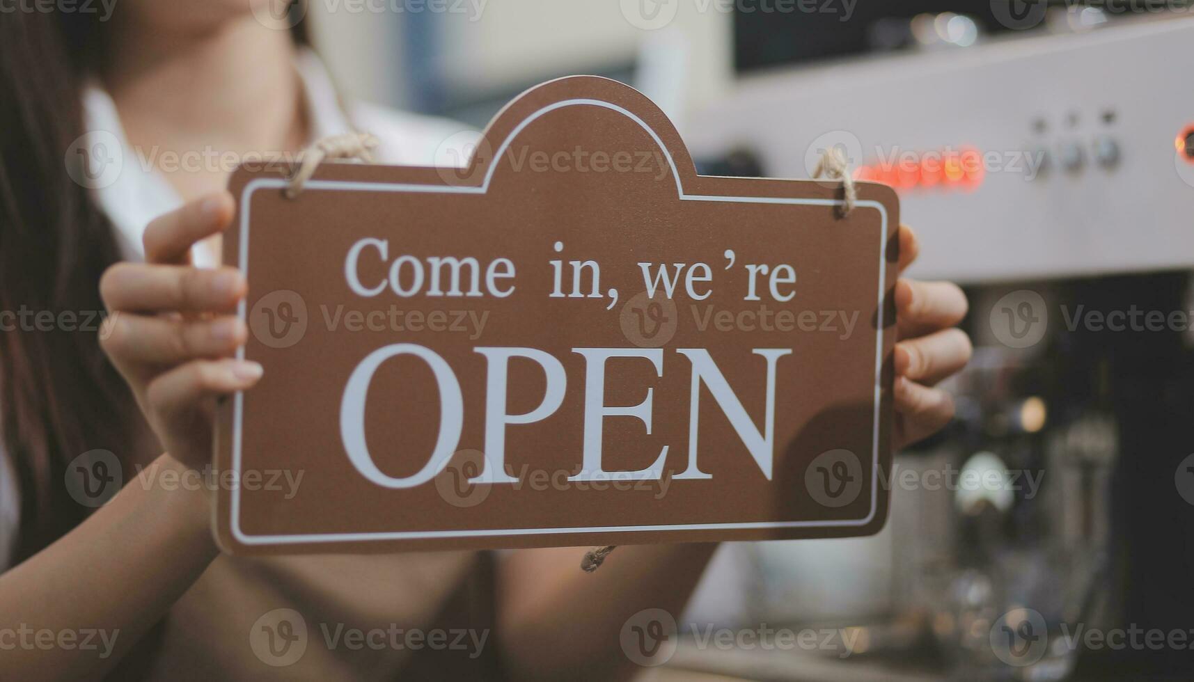 Bienvenue. ouvert. barman, serveuse femme tournant ouvert signe planche sur verre porte dans moderne café café magasin prêt à service, café restaurant, vente au détail magasin, petit affaires propriétaire, nourriture et boisson concept photo