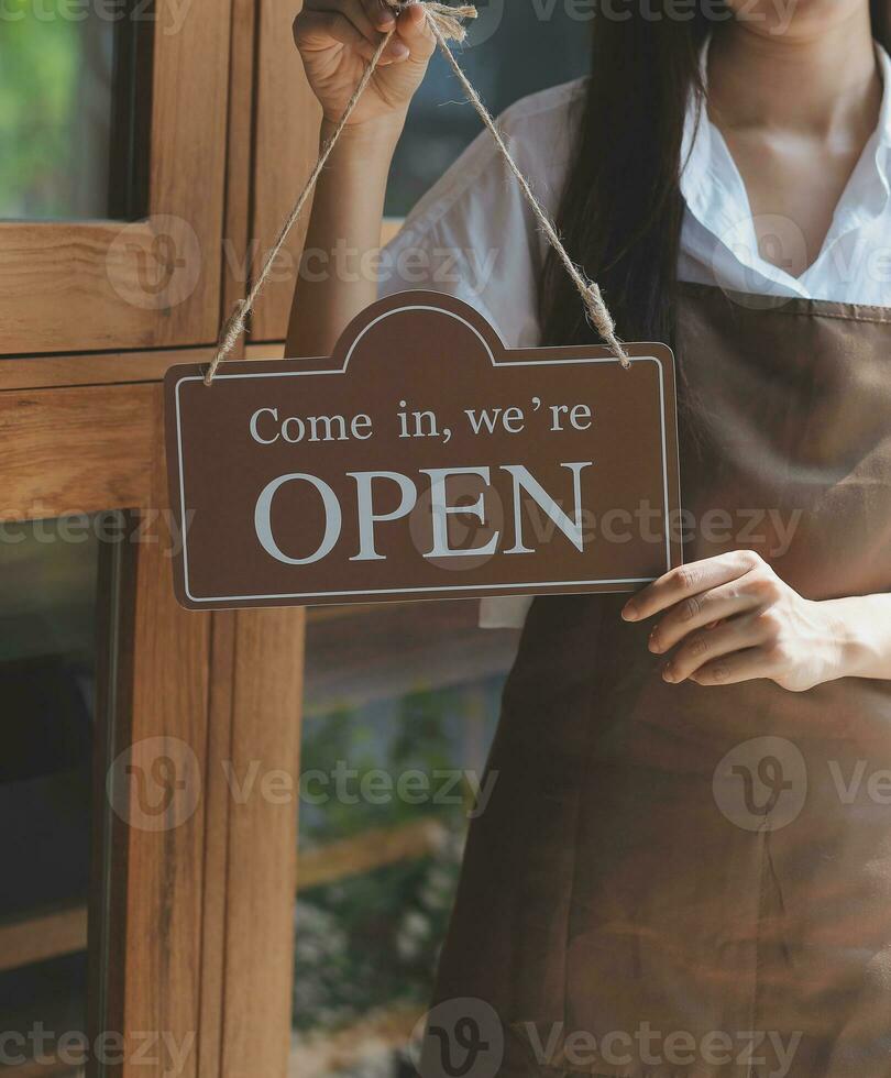 Bienvenue. ouvert. barman, serveuse femme tournant ouvert signe planche sur verre porte dans moderne café café magasin prêt à service, café restaurant, vente au détail magasin, petit affaires propriétaire, nourriture et boisson concept photo