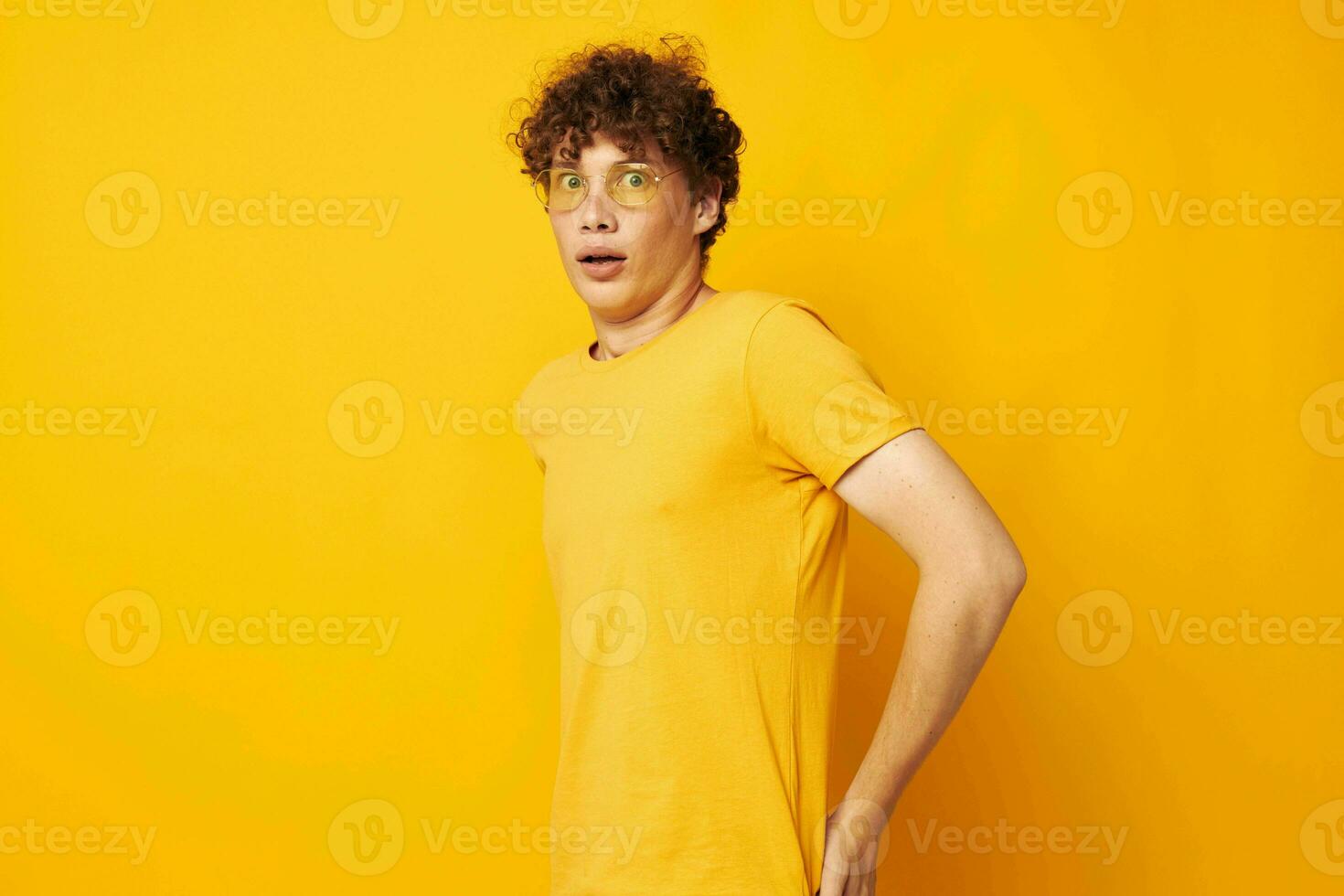 gars avec rouge frisé cheveux portant élégant des lunettes Jaune T-shirt posant isolé Contexte inchangé photo