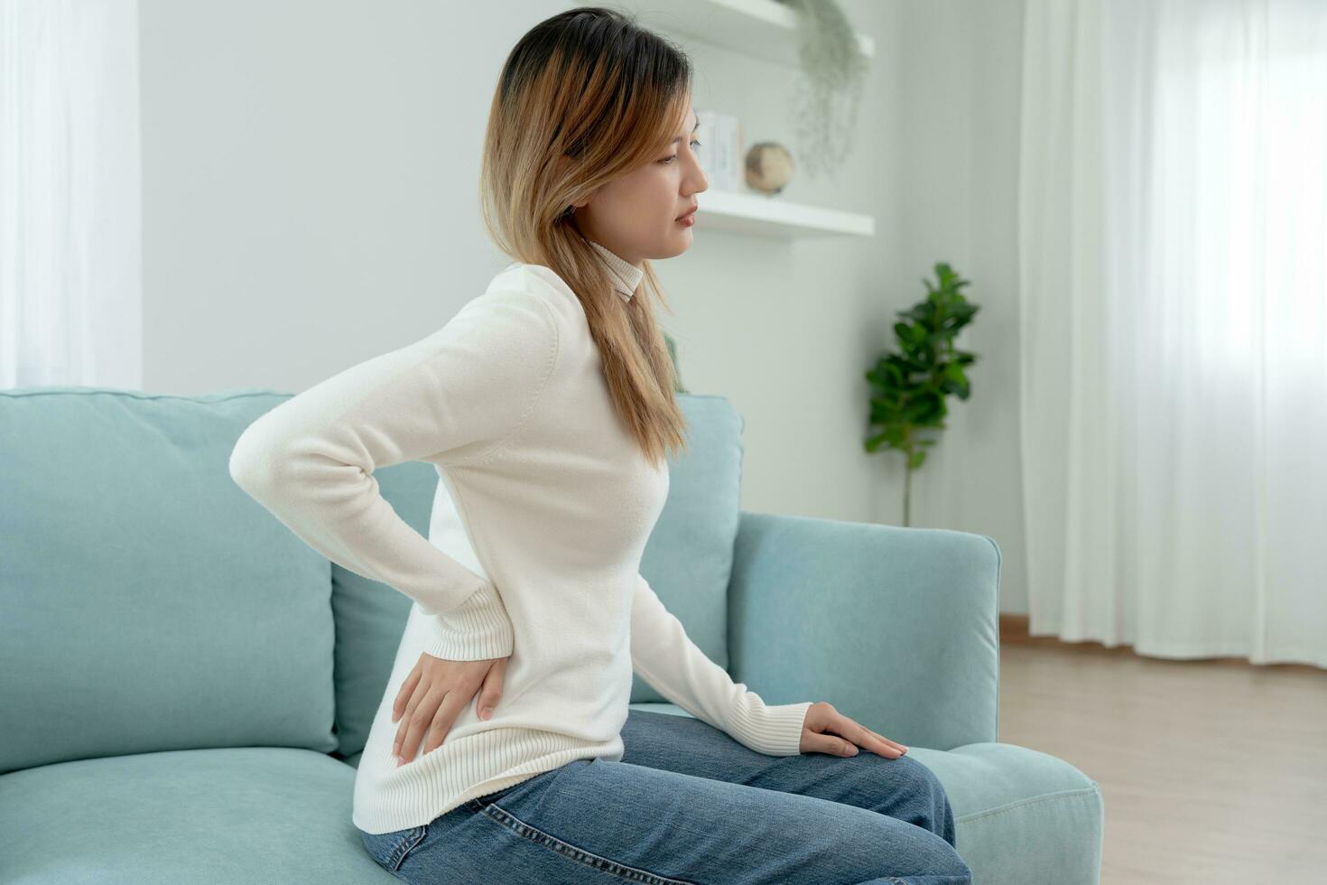 Asie magnifique femme en portant sa inférieur retour tandis que et souffrir de insupportable douleur santé et problèmes, chronique retour douleur, mal au dos dans Bureau syndrome, scoliose, hernie disque, muscle inflammation photo