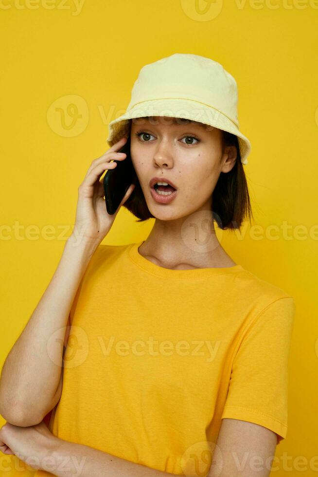 attrayant femme Jaune T-shirt et chapeau été style avec téléphone isolé Contexte photo