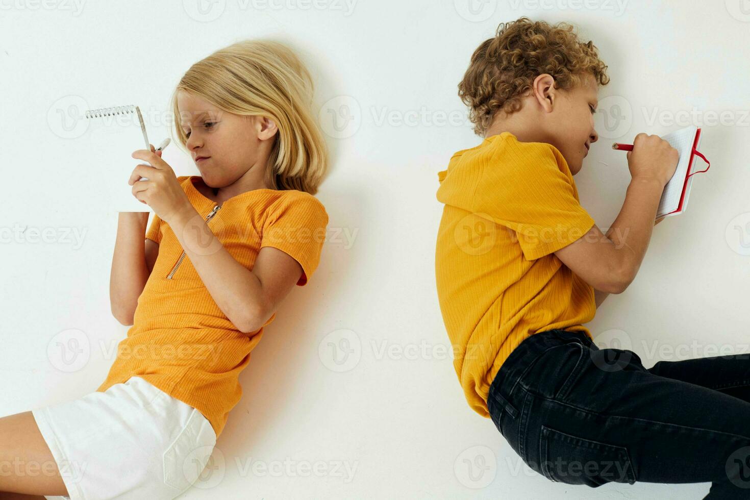 image de positif garçon et fille mensonge sur le sol avec blocs-notes et des crayons isolé Contexte inchangé photo
