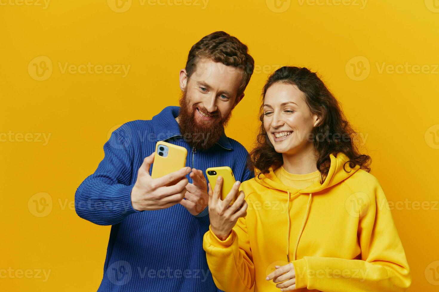 homme et femme couple souriant joyeusement avec téléphone dans main social médias visualisation Photos et vidéos, sur Jaune arrière-plan, symboles panneaux et main gestes, famille pigistes.