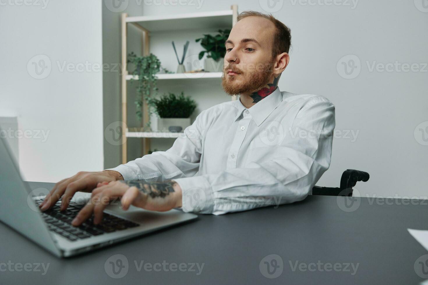 une homme dans une fauteuil roulant une homme d'affaire avec tatouages dans le Bureau travaux à une ordinateur portable, l'intégration dans société, le concept de travail une la personne avec handicapées, liberté de social cadres photo