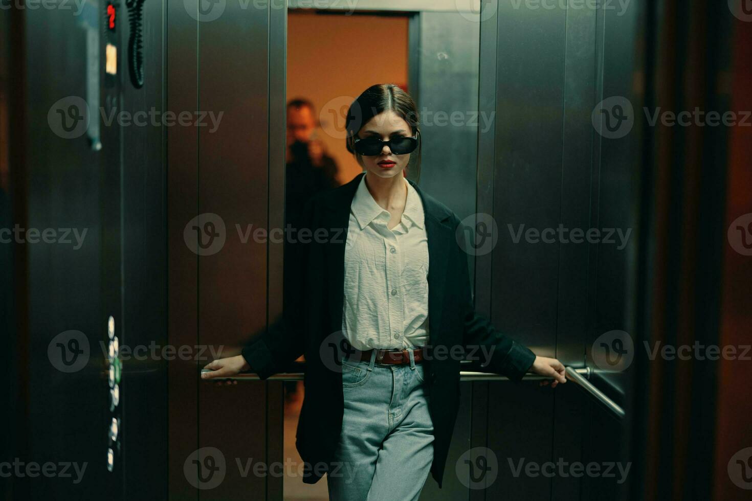 élégant femme dans noir veste et des lunettes de soleil posant dans ascenseur, mode modèle, foncé cinématique lumière et couleur, charme ancien photo