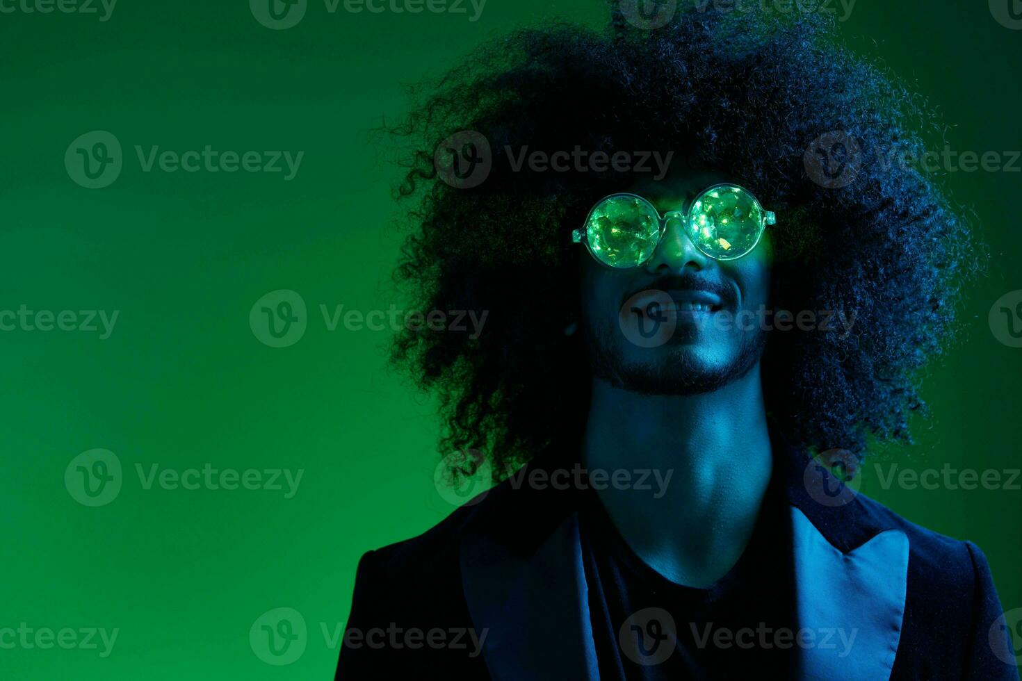mode portrait de une homme avec frisé cheveux sur une vert Contexte avec des lunettes de soleil, multinational, coloré rose lumière, branché, moderne concept. photo