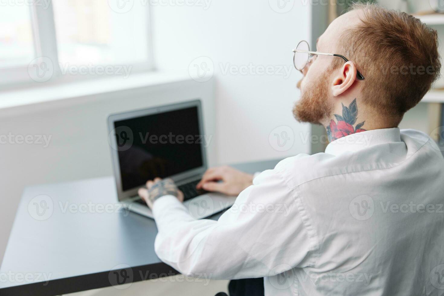 une homme fauteuil roulant homme d'affaire avec tatouages Bureau travaux à une portable en ligne, social réseaux et Commencez, l'intégration dans société, le concept de travail une la personne avec handicapées, vue de le retour photo