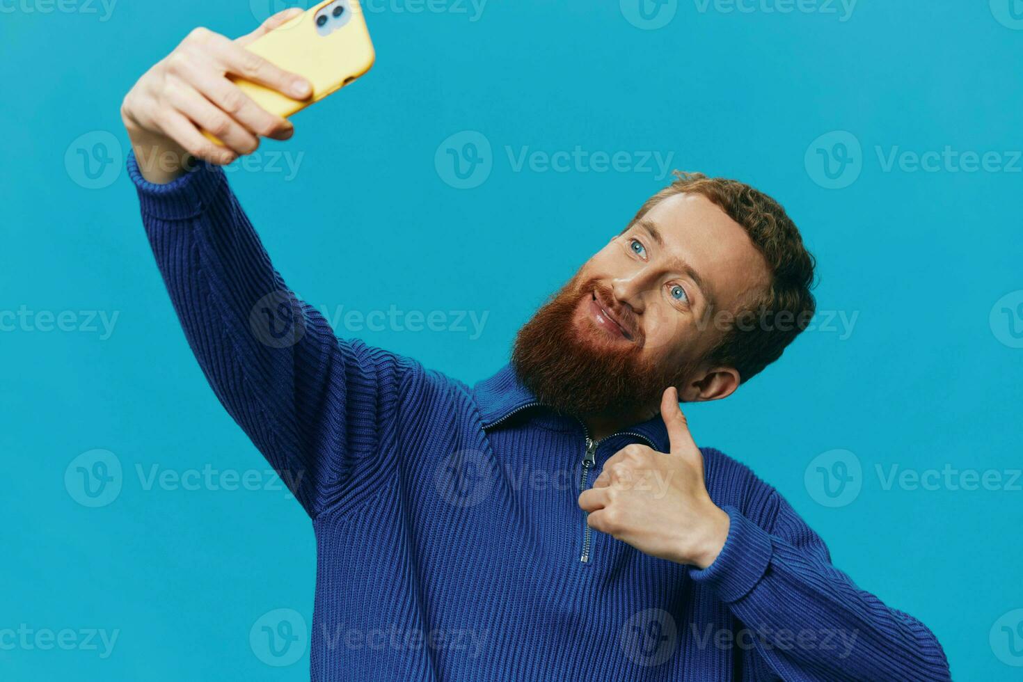 portrait de une homme avec une téléphone dans le sien mains blogueur prend selfies, sur une bleu Contexte. communicant en ligne social médias, mode de vie photo