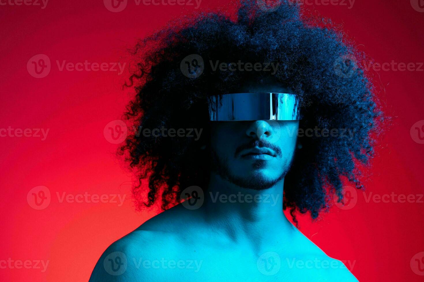 portrait de mode homme avec frisé cheveux sur rouge Contexte avec élégant lunettes, multinational, coloré lumière, noir cuir veste s'orienter, moderne concept, sexy corps. photo