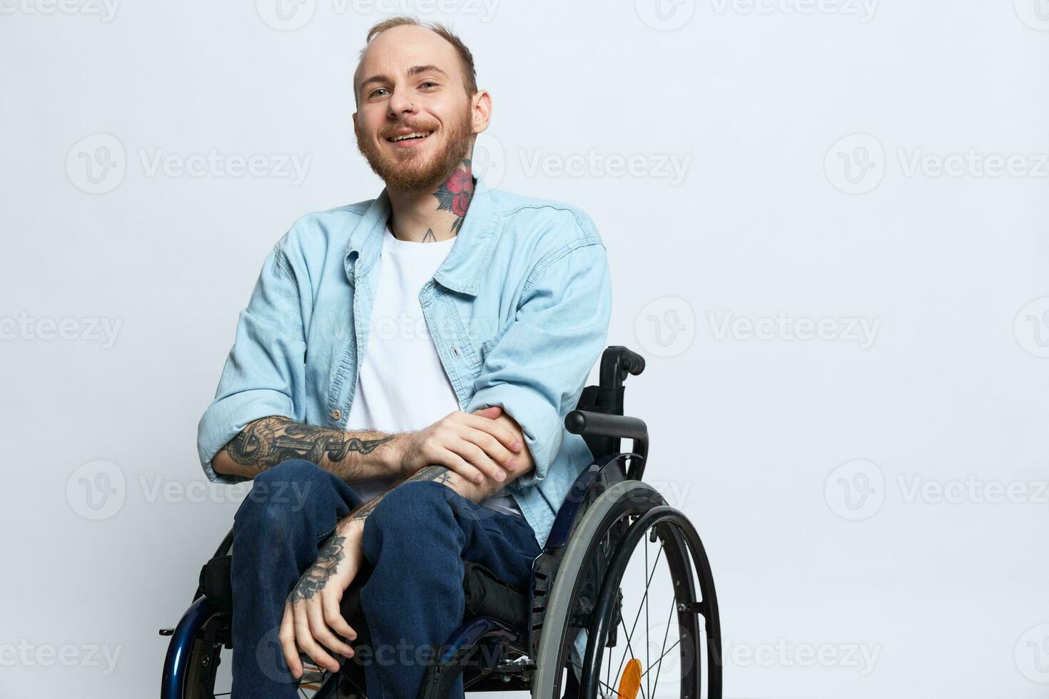 une homme dans une fauteuil roulant sourire, copie espace, avec tatouages sur le sien bras est assis sur une gris studio arrière-plan, le concept de santé est une la personne avec handicapées, une réel la personne photo
