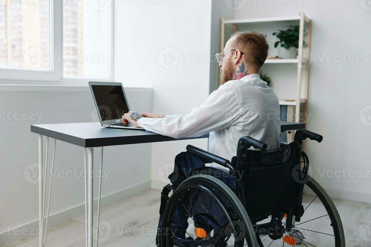 une homme dans une fauteuil roulant regards à le caméra homme d'affaire dans le Bureau travail sur une portable en ligne, social réseaux Commencez, l'intégration dans société, concept travail la personne avec handicapées, vue retour photo