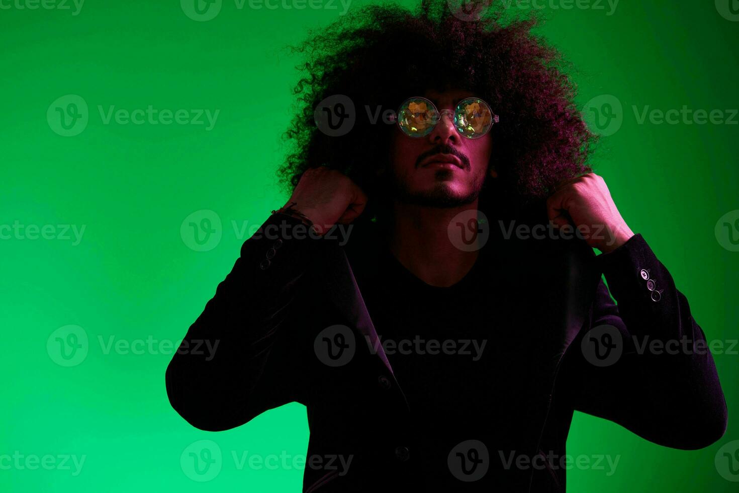 mode portrait de une homme avec frisé cheveux sur une vert Contexte avec des lunettes de soleil, multinational, coloré rose lumière, branché, moderne concept. photo