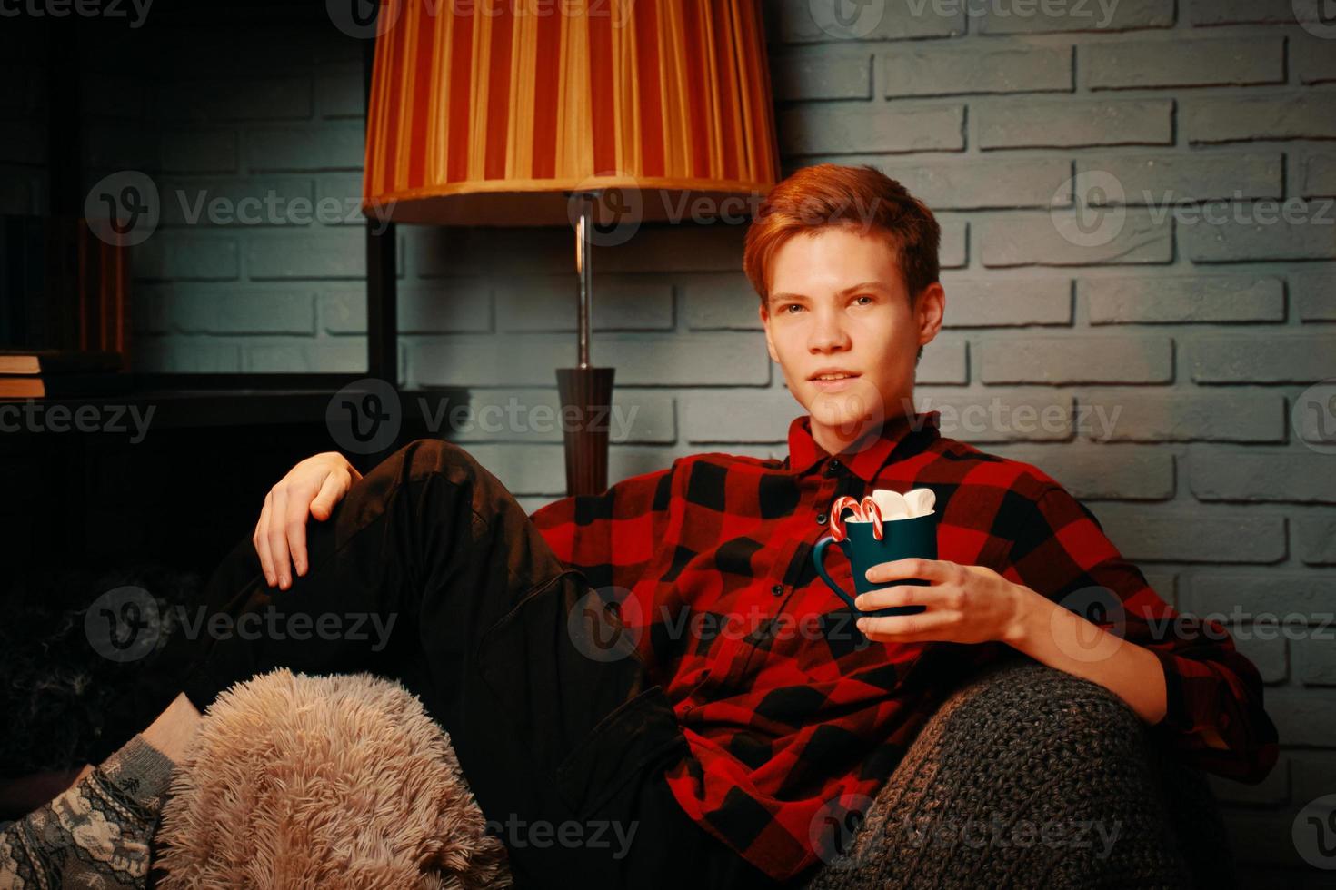 Bel homme dans une chaise tient une tasse de chocolat chaud avec des guimauves photo