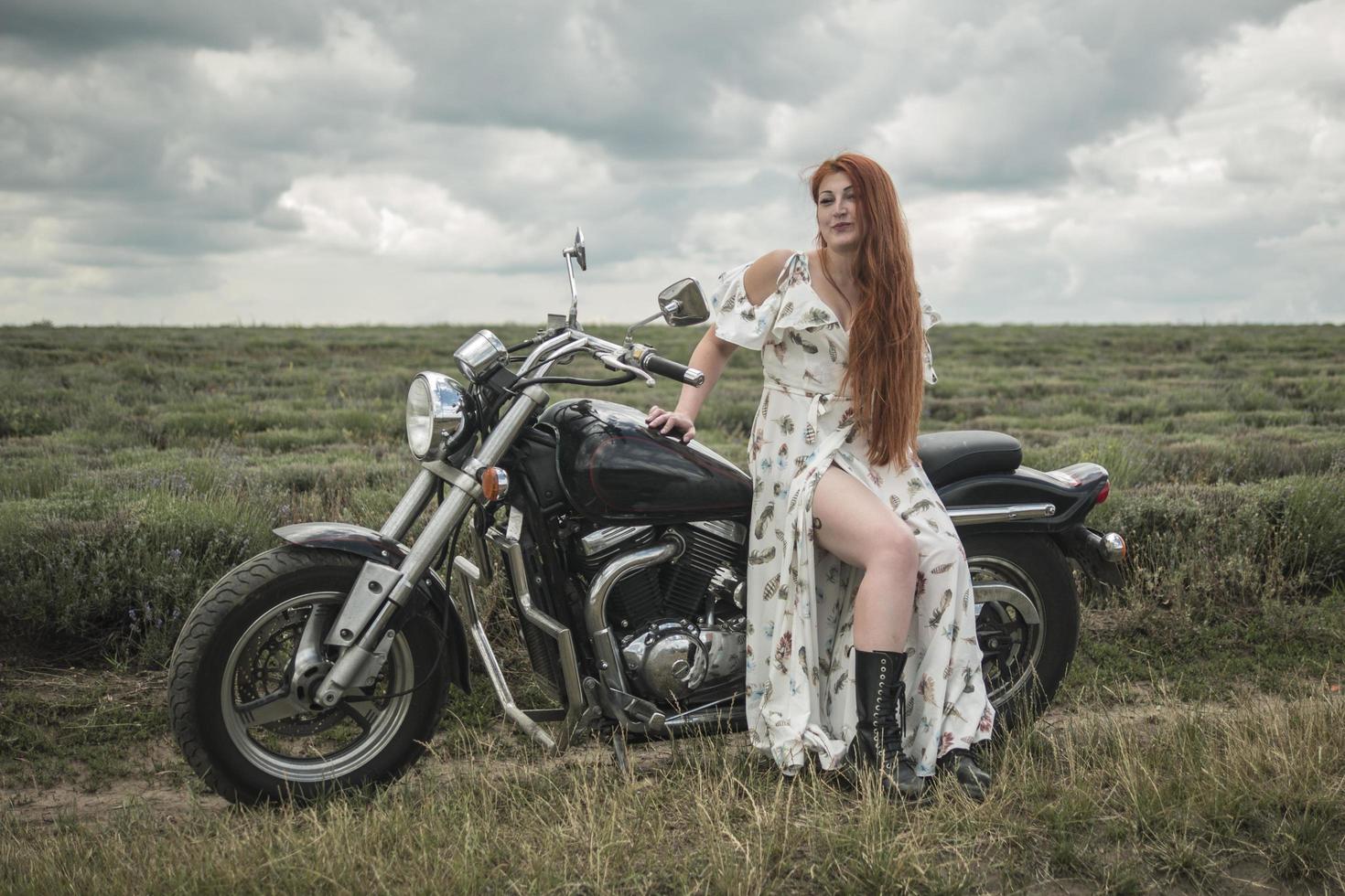 Fille aux cheveux rouges dans une robe blanche et des bottes avec un champ de lavande moto photo