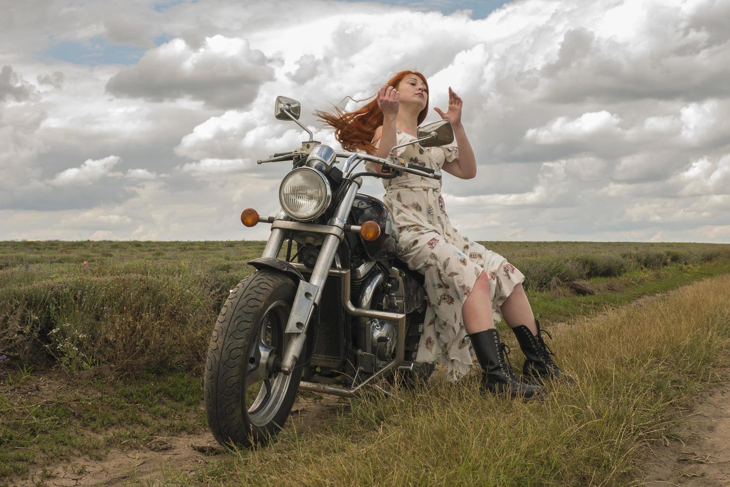 Fille aux cheveux rouges dans une robe blanche et des bottes avec un champ de lavande moto photo