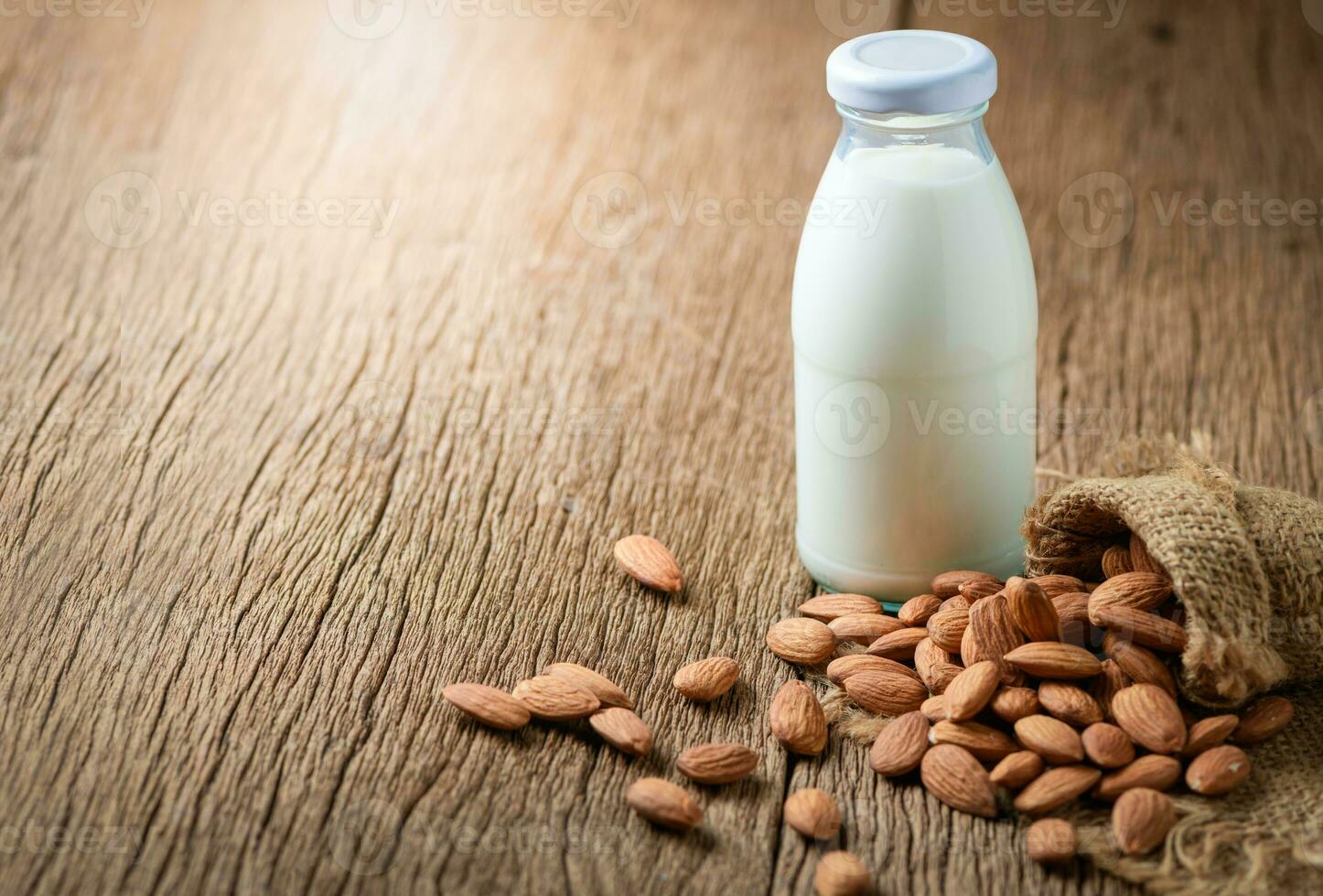 bouteille de Frais Lait et amandes des noisettes dans sac sur bois table Contexte. photo