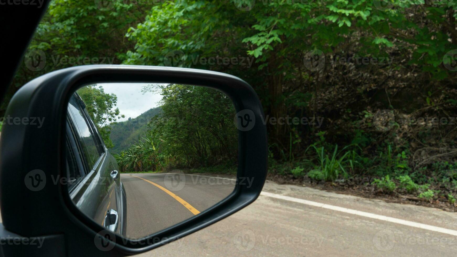 miroir vue de gris voiture Voyage sur le asphalte route. avec flou de vert forêt à côté de route à journée. photo